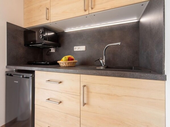 Una cocina moderna con armarios de madera, campana extractora de acero inoxidable, lavavajillas integrado y una cesta de frutas en la encimera.