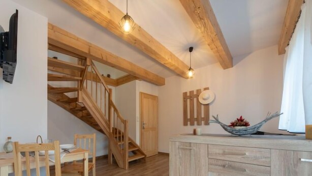 Una cocina rústica con vigas de madera, una escalera de madera y un comedor con sillas y una mesa.
