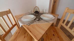 Una mesa de madera para comer con dos platos, cubiertos y vasos.