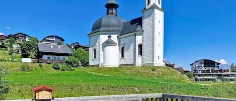 A church with two domes and a bell tower, surrounded by houses and a wooden deck with a bench.