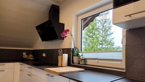 Una cocina moderna con armarios blancos, encimera negra y ventana con vistas a árboles.