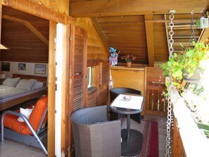 A cozy cabin interior with a bed, a small table, wicker chairs, and a hanging plant.