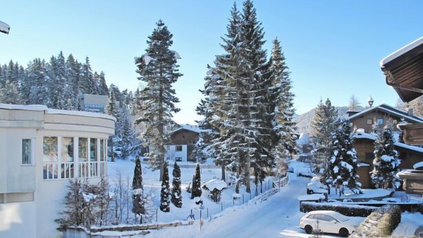 Zona residencial cubierta de nieve con casas, un edificio curvo con ventanas grandes y un cielo despejado.
