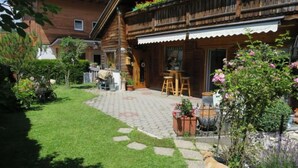 Una casa de madera con un patio empedrado, mobiliario de exterior y un perro.