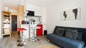 A modern kitchen with a red refrigerator, white cabinets, and a stainless steel microwave. There are two bar stools with red seats and a blue sofa with fluffy pillows. - WELCS ESTUDIO 070 EMP frente al Mar (Empuriabrava)