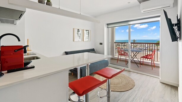 A modern kitchen with a white countertop, red bar stools, and a view of the ocean through large sliding doors. - WELCS ESTUDIO 070 EMP frente al Mar (Empuriabrava)
