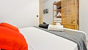 A neatly made bed with a white and gray blanket, two pillows, and a small towel with flowers. A wooden wardrobe is visible in the background. - WELCS ESTUDIO 070 EMP frente al Mar (Empuriabrava)