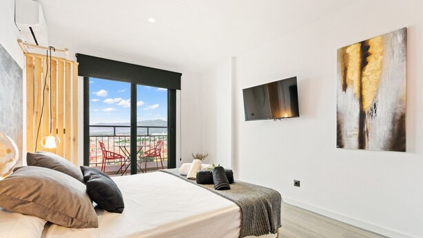 Ein modernes Schlafzimmer mit einem großen Bett, einem an der Wand montierten Fernseher und einem Balkon mit Blick auf die Stadt.