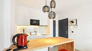 Eine moderne Küche mit einer Holzauszug und einem roten Wasserkocher sowie einer schwarzen Kaffeemaschine. Über der Arbeitsfläche befinden sich drei Pendelleuchten.