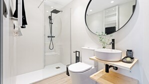 Ein modernes Badezimmer mit einer gläsernen Duschkabine, einer weißen Toilette, einem runden Spiegel und einem hölzernen Waschtisch.