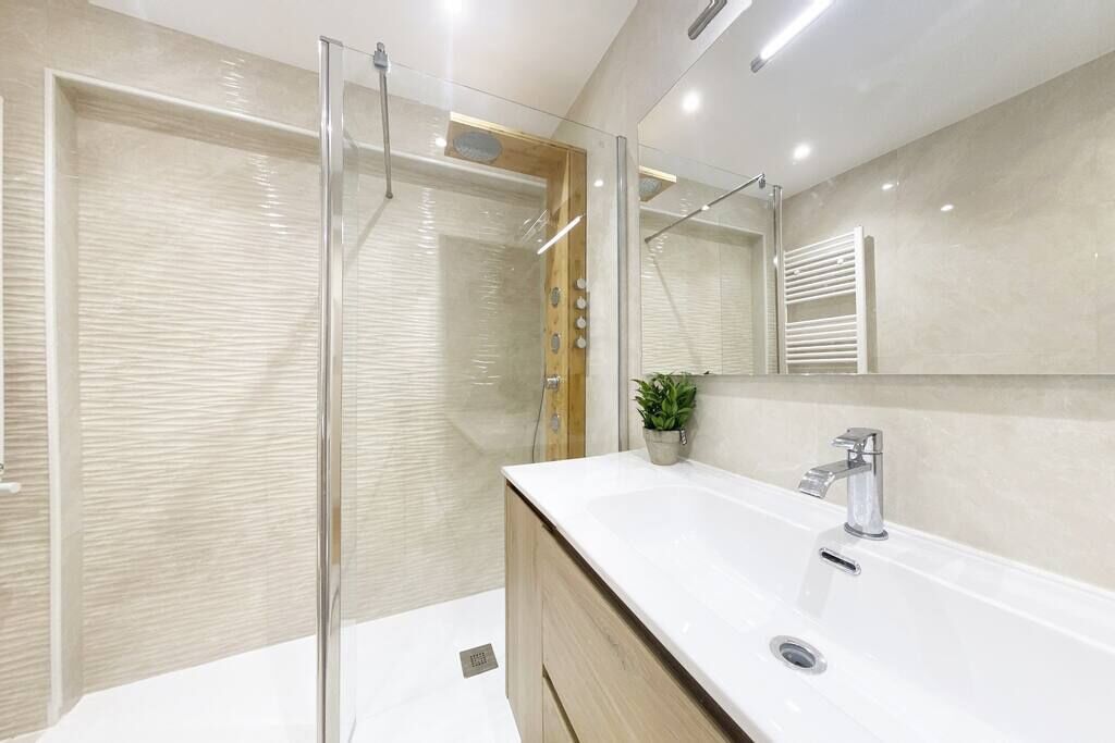 Un bagno moderno con doccia vetrata, lavandino bianco con specchio e mobile contenitore in legno.