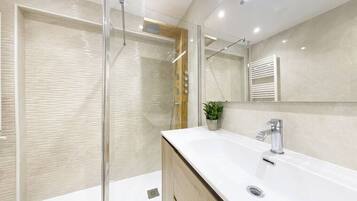 Un bagno moderno con doccia vetrata, lavandino bianco con specchio e mobile contenitore in legno.