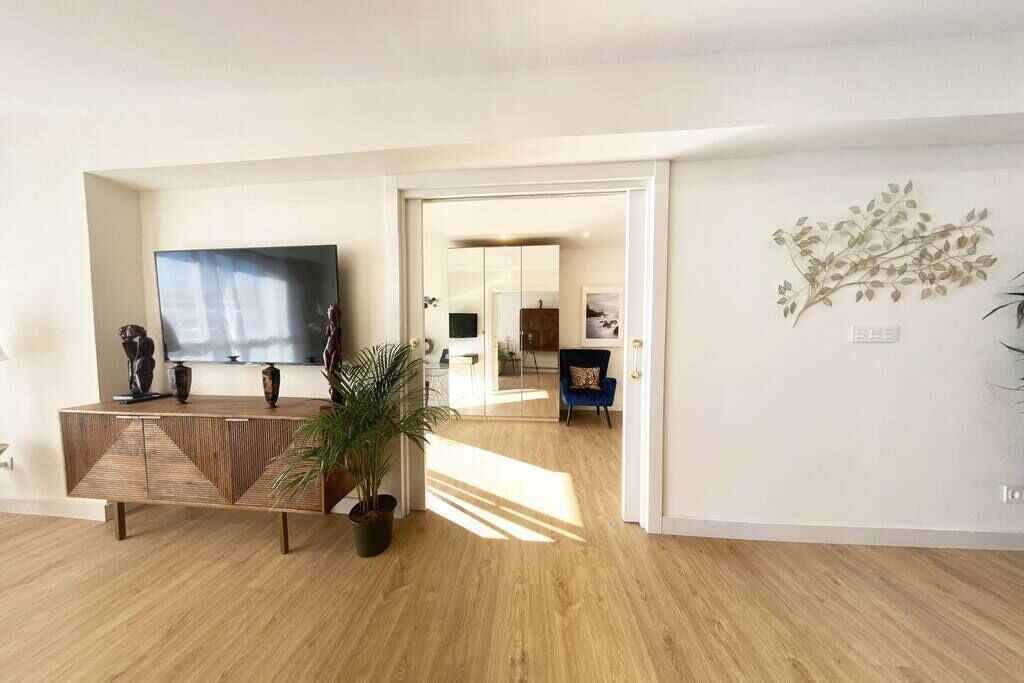 Un salón moderno con suelo de madera, un televisor plano grande, un mueble decorativo y una planta en maceta.