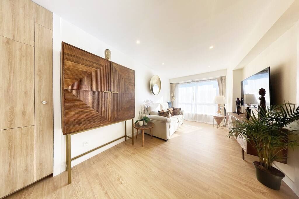 Una sala de estar moderna con un mueble grande de madera, un espejo redondo, un sofá, una mesa de centro y un televisor.