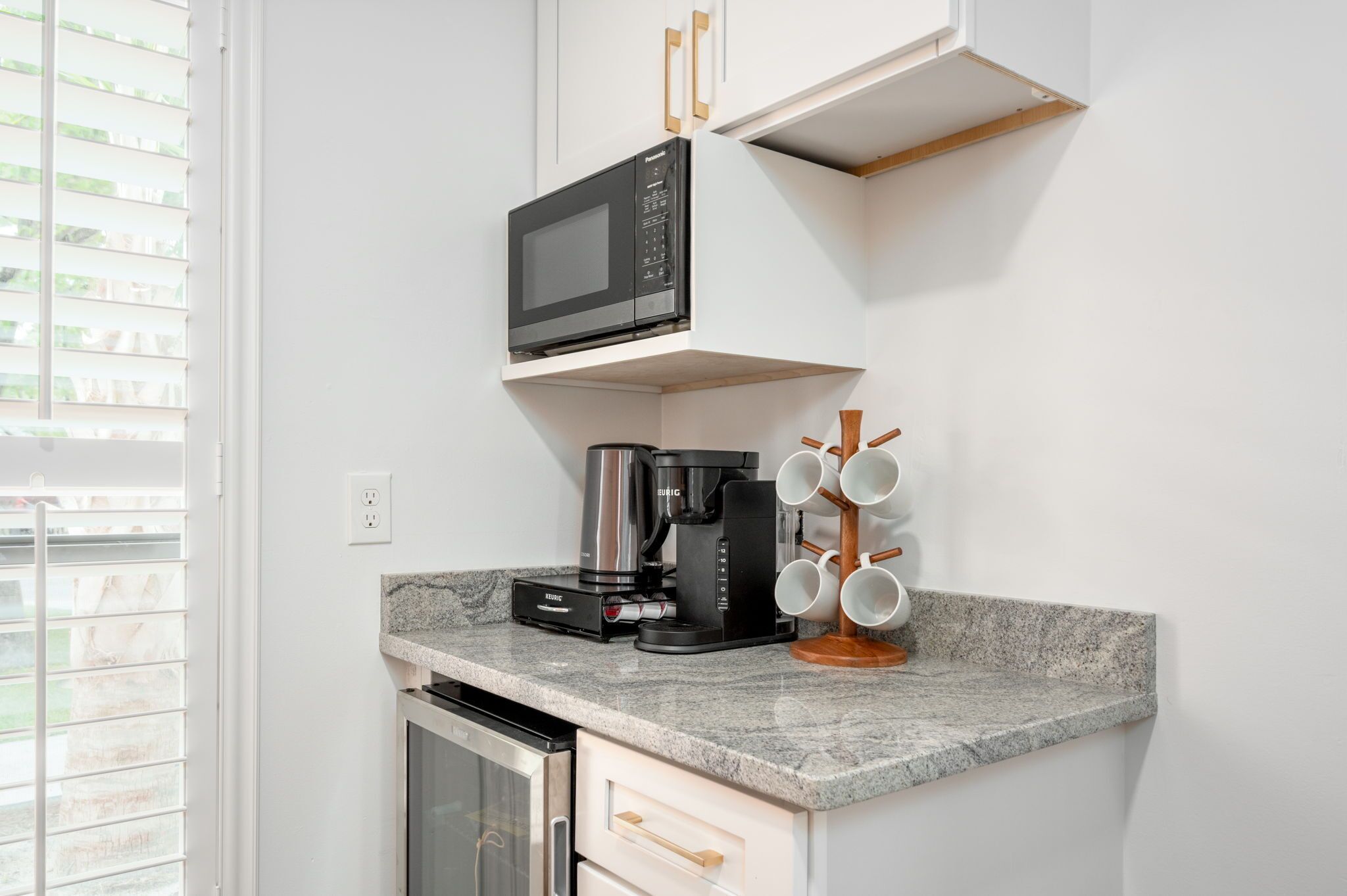 A compact kitchen with a built-in microwave, coffee maker, and a mug holder.