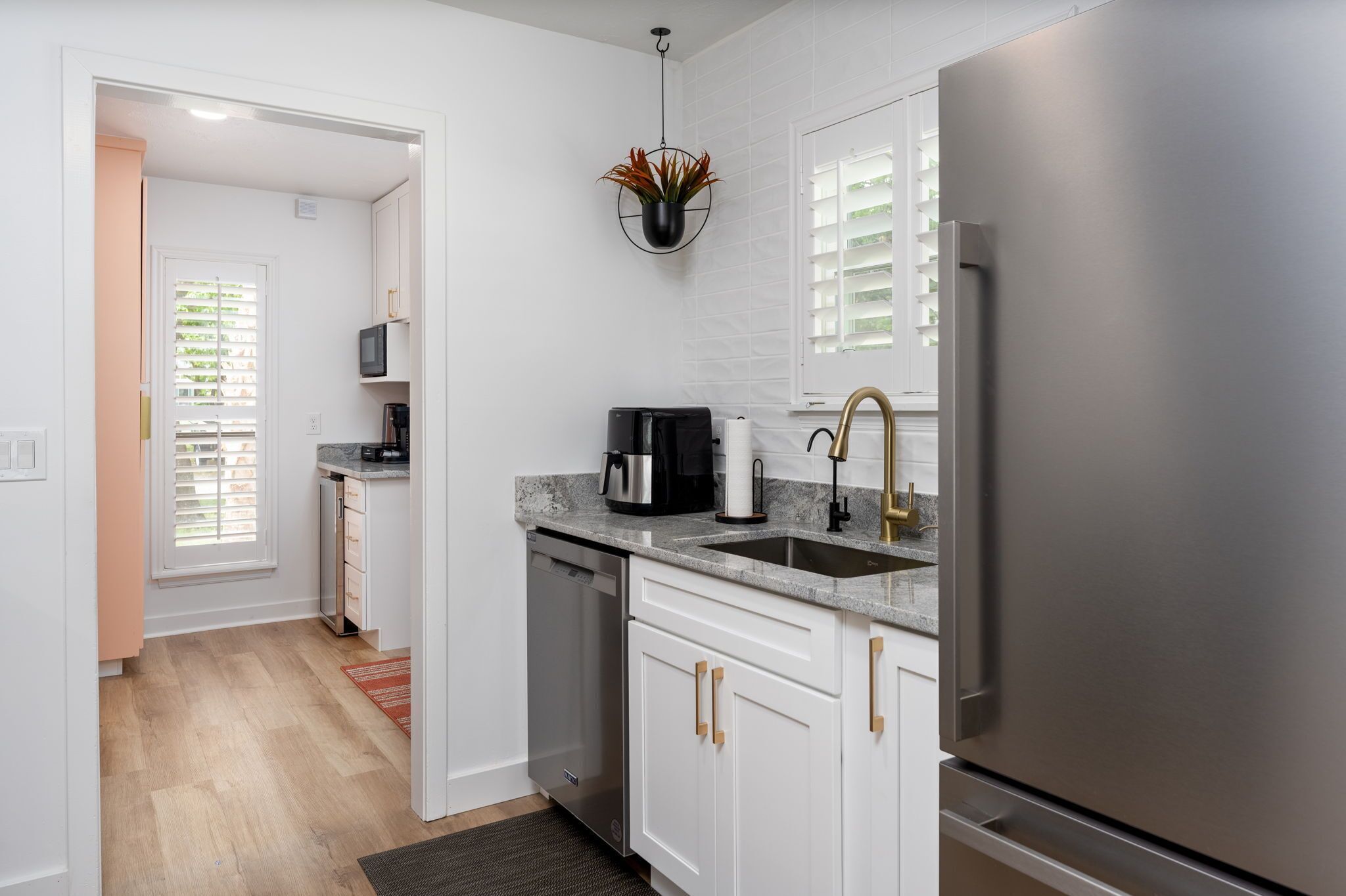 A modern kitchen with white cabinetry, a stainless steel refrigerator, a coffee maker, and a hanging plant.