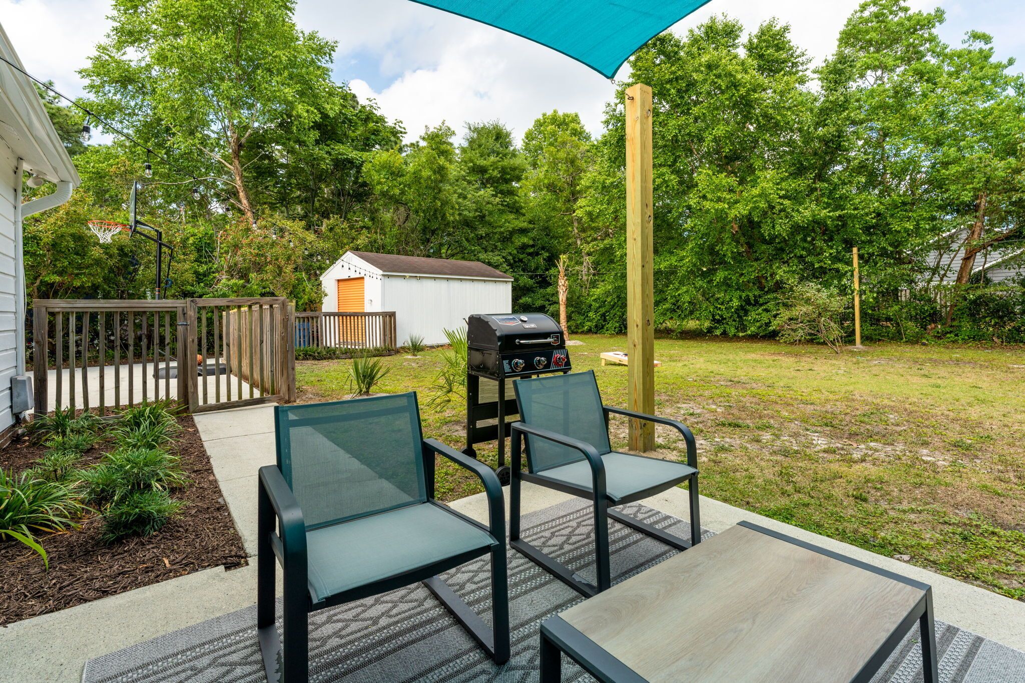 En udendørs terrasse med et bord, stole, grill og et overdækket område.