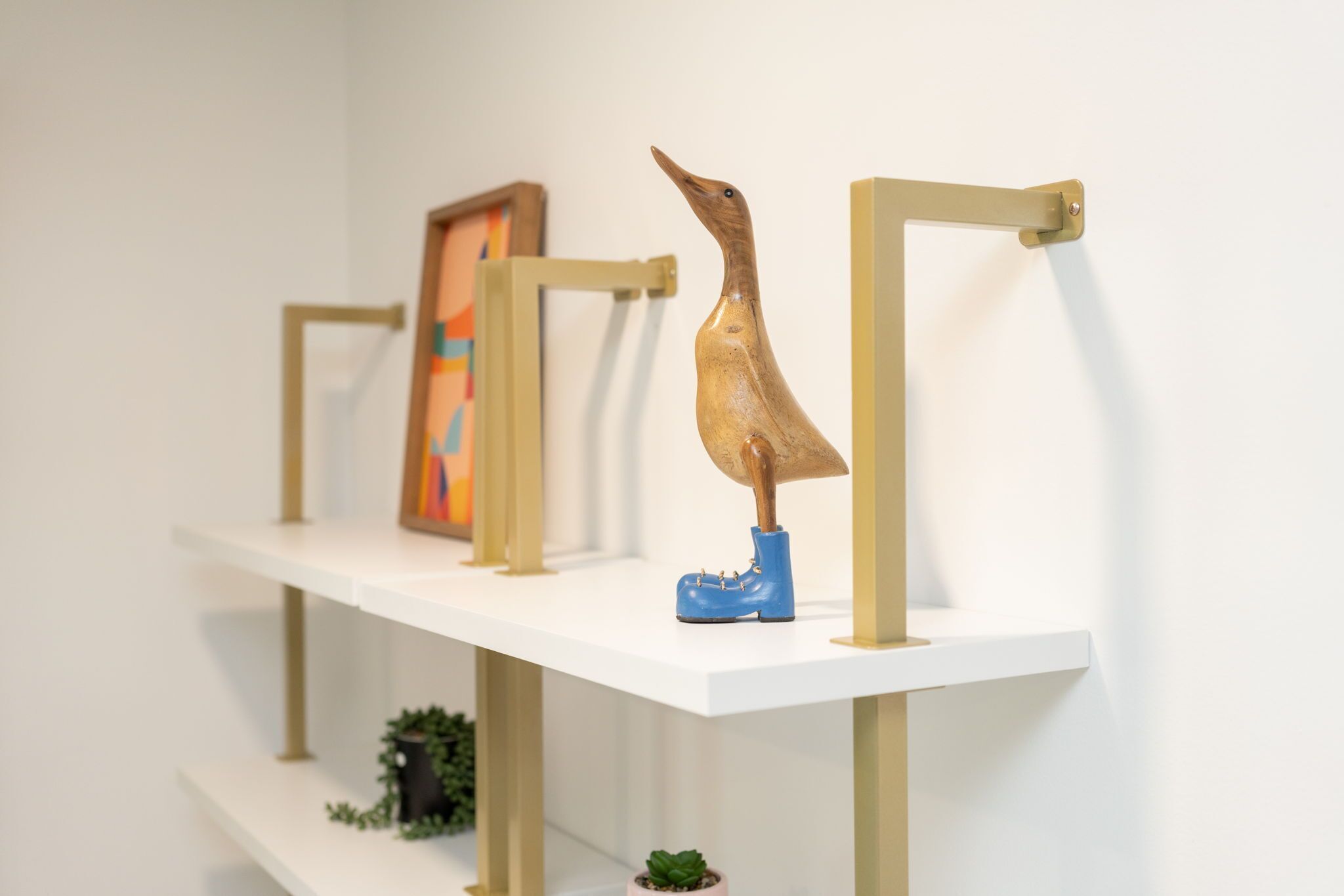 Un estante blanco con una escultura de madera y un cuadro enmarcado.