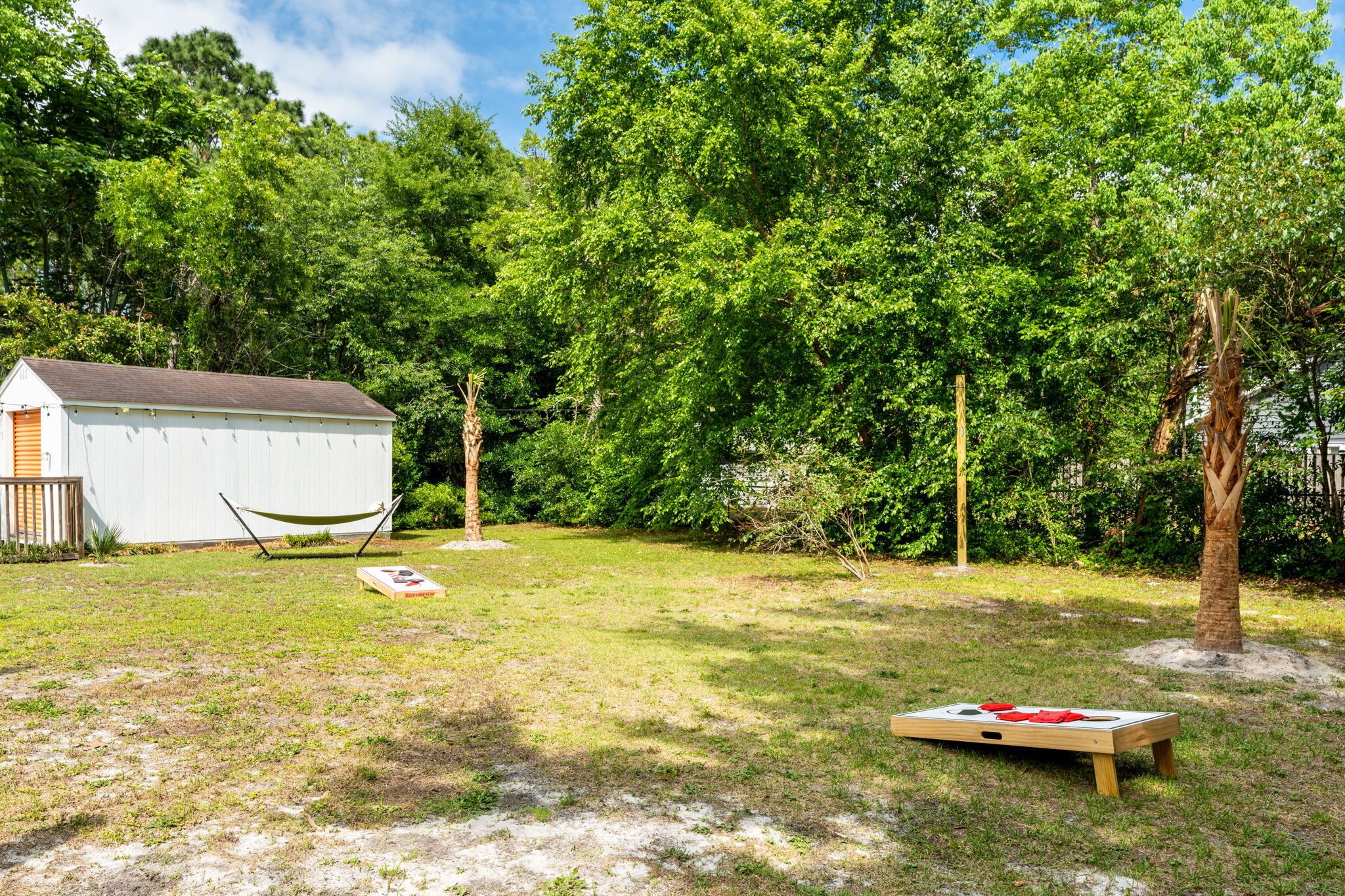 A backyard with a white shed, a hammock, and a picnic table with red cushions.