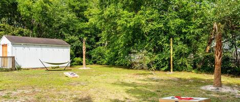 A backyard with a white shed, a hammock, and a picnic table with red cushions.