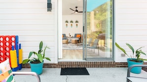 Entrada de casa com porta de vidro deslizante, ventilador de teto e um pequeno pátio com móveis de exterior e plantas em vasos.