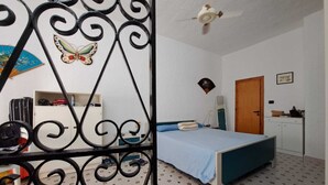 Un dormitorio con cama, ventilador de techo, armario, escritorio y una puerta.