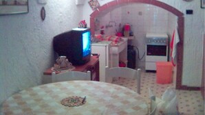 Cocina compacta con comedor, destacando un rebozado de azulejos, un horno pequeño y un televisor sobre un mueble de madera.