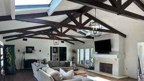 Ein großzügiges Wohnzimmer mit hoher Decke, Holzbalken, einem Kamin, einem großen Sofa und einem Fernseher.