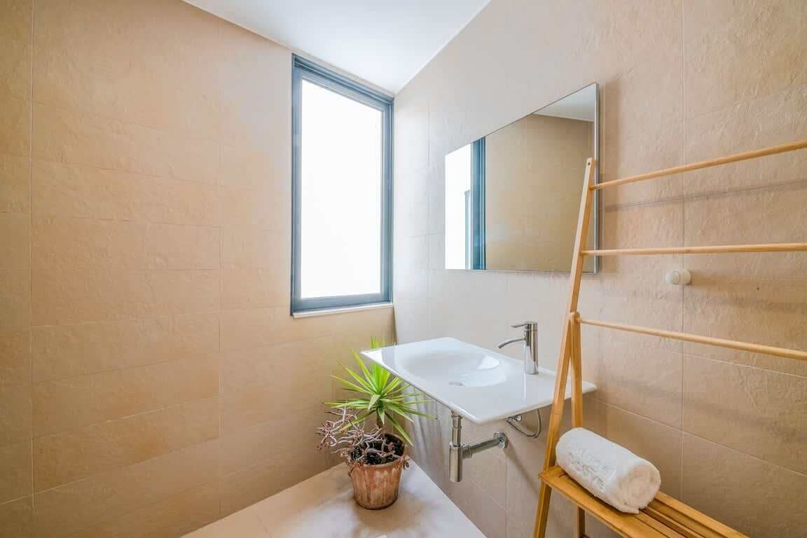 A modern bathroom with a large window, a sink, a mirror, a towel rack, and a potted plant.