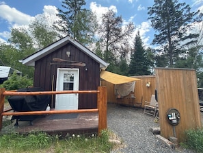 Une cabane en bois avec une porte portant le numéro « 11 », une terrasse en bois, un barbecue et une petite table avec des chaises.