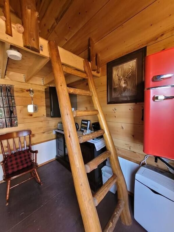 A wooden interior with a ladder, a red refrigerator, and a deer picture on the wall.