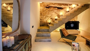 A staircase with a stone wall backdrop, a flat-screen TV, and a cozy seating area with a magazine. - Cave Suite COVA (Cave Hotel Lomas de Ruvira) (Jorquera)
