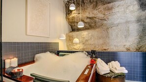 A spa bath with bubbles, a stone wall, and a blue-tiled wall. - Cave Suite COVA (Cave Hotel Lomas de Ruvira) (Jorquera)