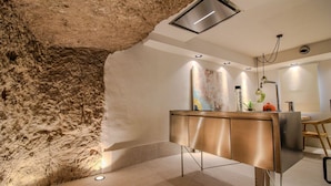 A modern bathroom with a stone wall, a stainless steel vanity, recessed lighting, and a ceiling light fixture. - Cave Suite COVA (Cave Hotel Lomas de Ruvira) (Jorquera)