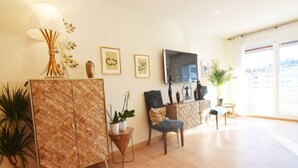 A modern living room with a wooden cabinet, a blue armchair, a small table, and a TV mounted on the wall. - The Paradise: Luxurious flat, parking, jacuzzi, terrace, new (Donostia)