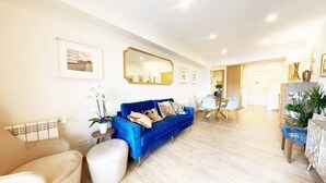 A spacious living room with a blue sofa, a white armchair, and a dining area with a table and chairs. - The Paradise: Luxurious flat, parking, jacuzzi, terrace, new (Donostia)