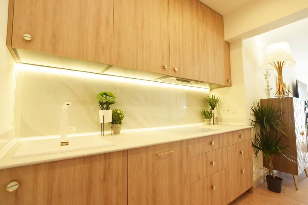 Una cocina moderna con armarios de madera, encimera blanca y plantas en macetas.