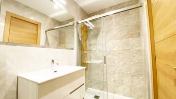 Un baño moderno con cabina de ducha de vidrio, tocador blanco y puerta de madera.