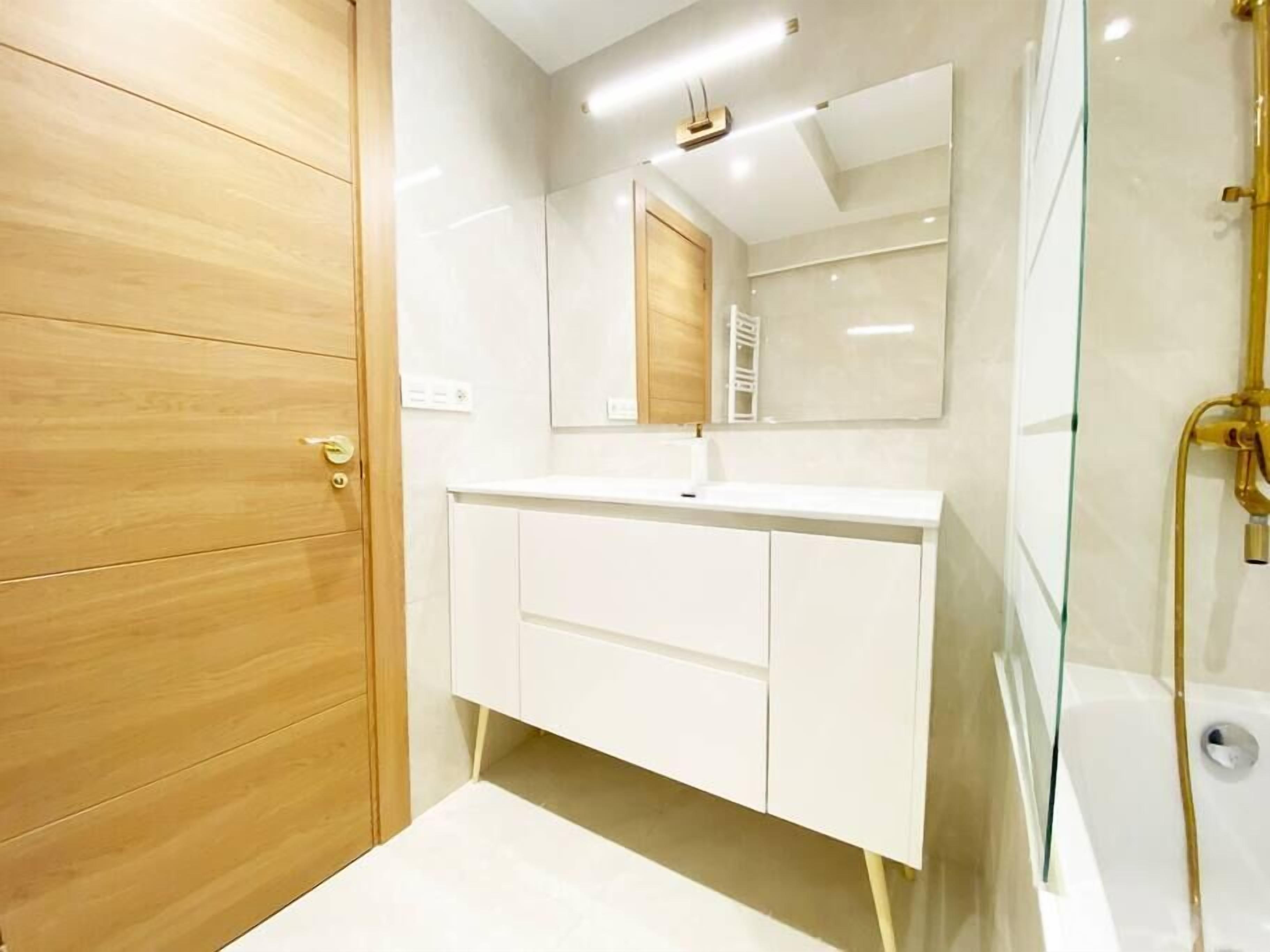 Een moderne badkamer met een houten deur, een witte wastafel en een douchecabine met glazen wanden.