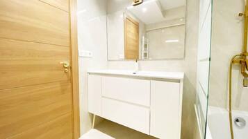 Een moderne badkamer met een houten deur, een witte wastafel en een douchecabine met glazen wanden.