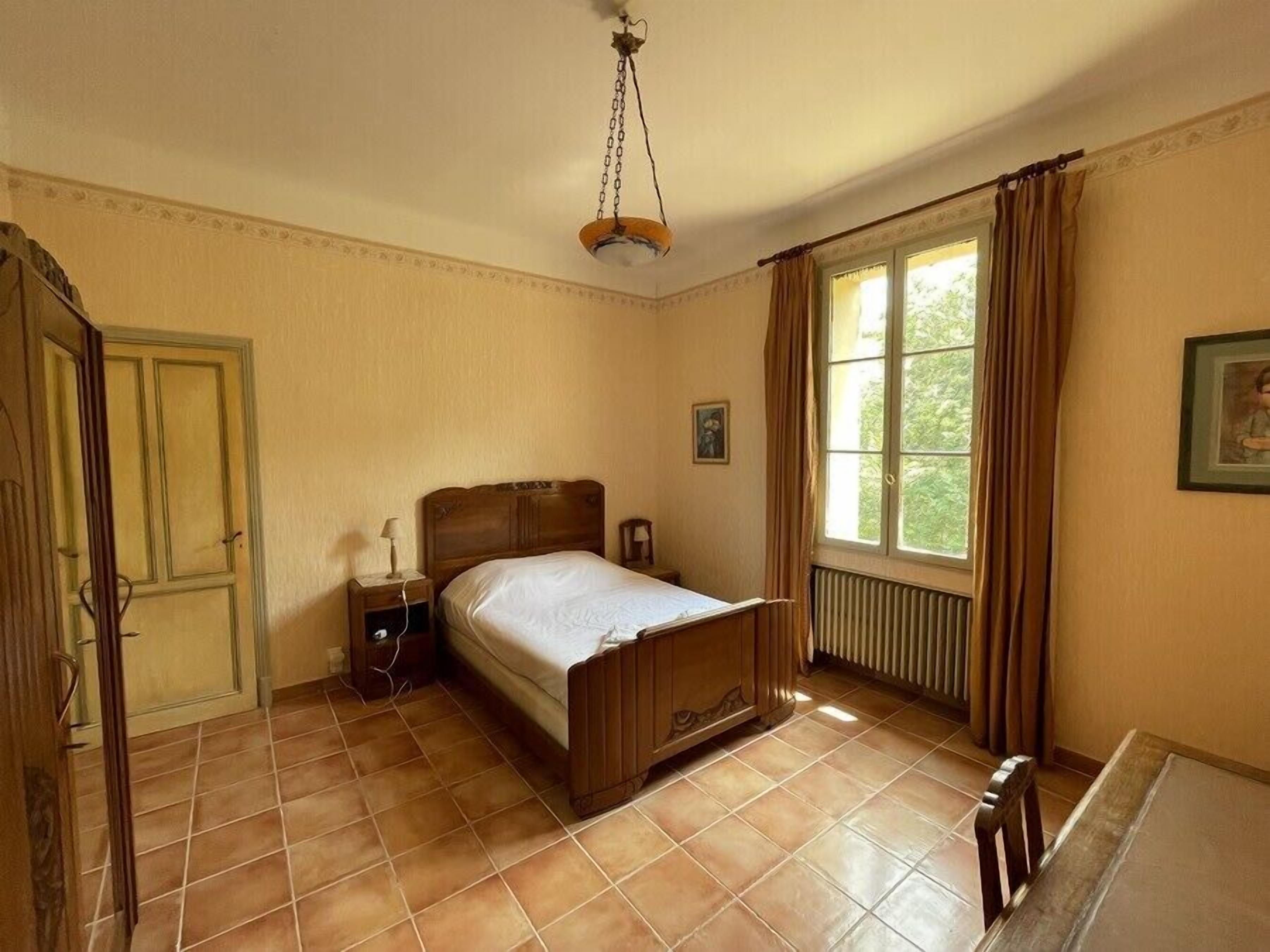 Ein Schlafzimmer mit einem hölzernen Bett, einem Nachttisch, einem Fenster mit Vorhängen und einer Heizung.