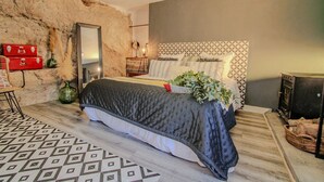 Une chambre à coucher avec une couvre-lit à motifs, une tête de lit ornée d’un motif géométrique, une commode rouge et un miroir.