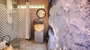 Une salle de bain avec un mur à motifs, un miroir rond, un lavabo et un espace douche.