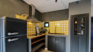 Une cuisine compacte avec un réfrigérateur noir, un crédence à carreaux jaunes et blancs, et une porte sombre dotée d’une fenêtre en treillis.