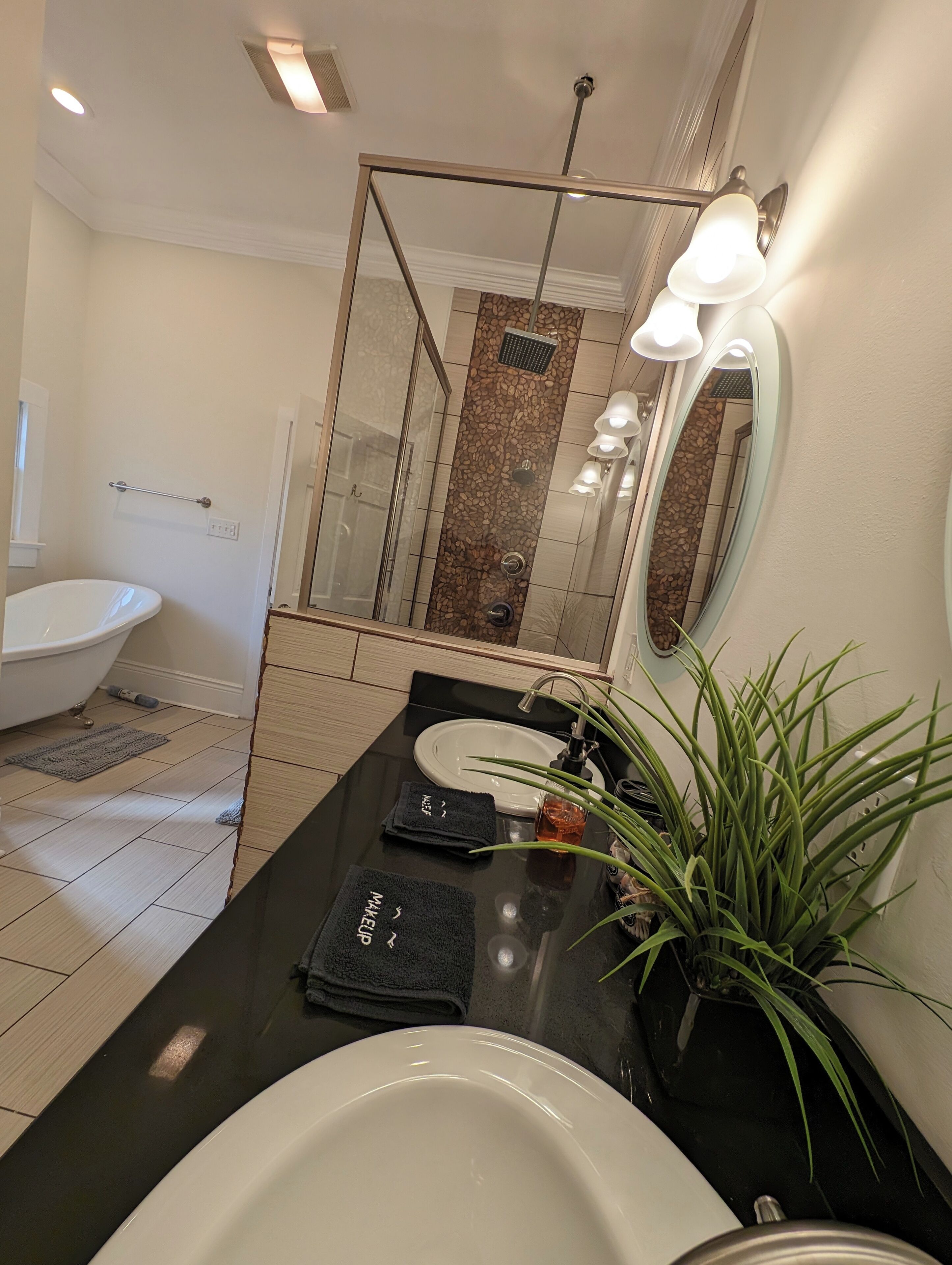 Un baño moderno con bañera, lavamanos, espejo y una planta en maceta.