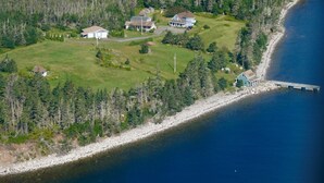 An aerial view of a coastal property with multiple houses, a dock, and a forested area.