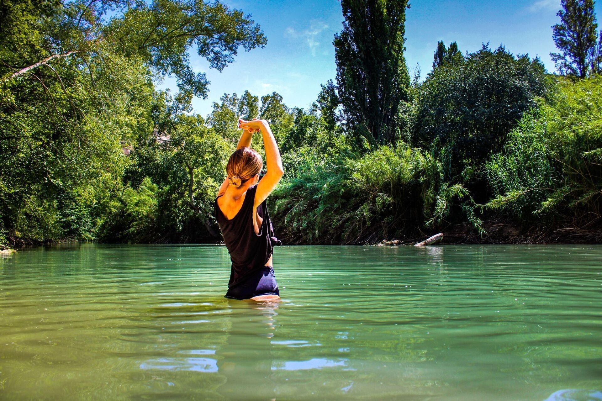 Een persoon doet yoga in een natuurlijke omgeving, met een rivier en weelderige begroeiing op de achtergrond.