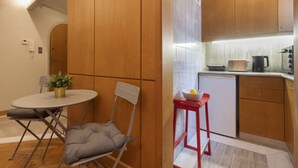 A compact kitchen with wooden cabinets, a small refrigerator, and a red stool.