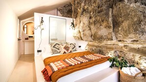 Une chambre avec un grand lit, un miroir, un mur en pierre et un luminaire suspendu.