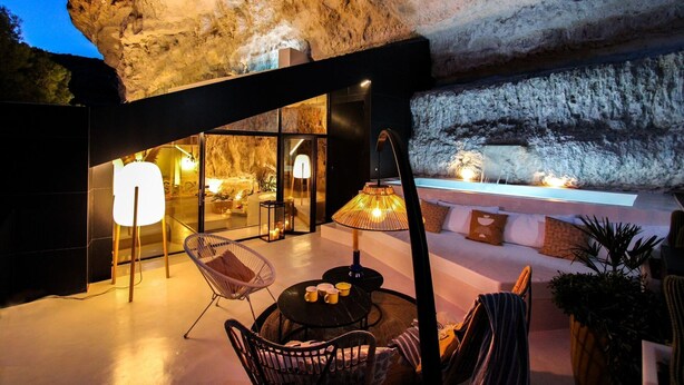 Un espace extérieur aménagé avec des sièges, offrant une vue sur une falaise rocheuse, une paroi en verre et une cascade.